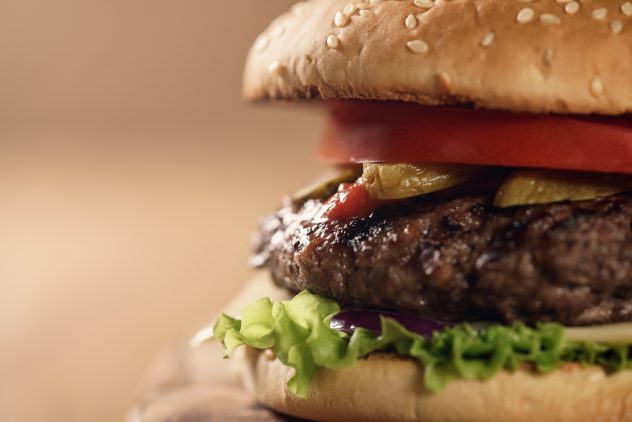 closeup fresh homemade burger with marble beef, cheese and vegetables on olive board