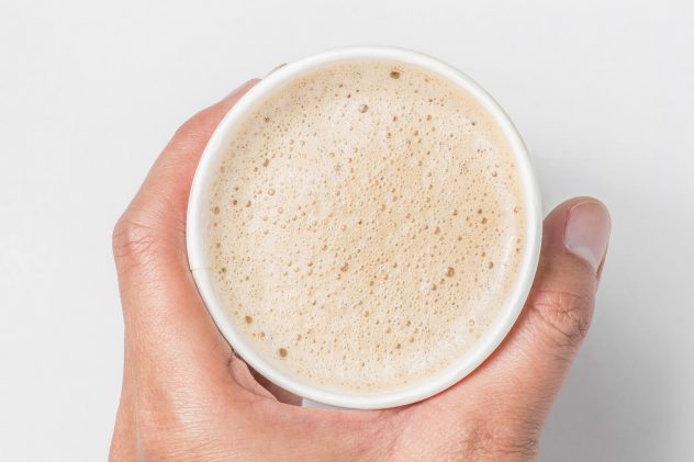 top view of hand holding paper cup mix latte coffee foam, white