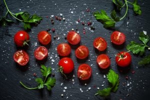Cut cherry tomatoes on a black background with spices, top view