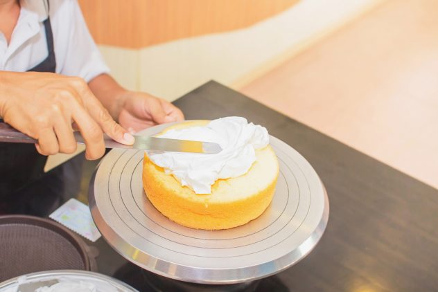 chef hand frosting a cake with whipped cream selective focus