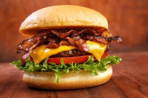 Ovatko nämä miehekkäimpiä ruoka-annoksia ikinä? Bacon burger with beef patty on red wooden table