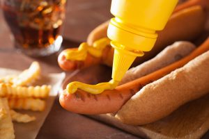 adding mustard to grilled hot dog