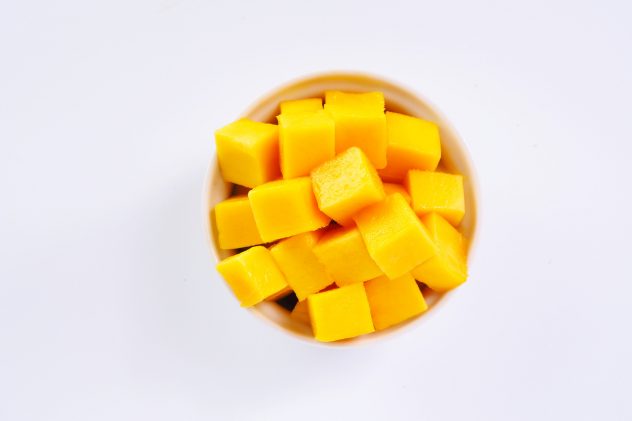 Top view of diced ripe mango cube in a white bowl on a white background.
