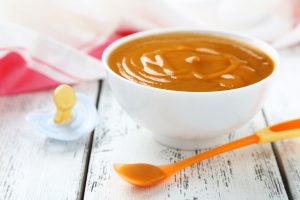 Baby food in bowl with spoon on white wooden background