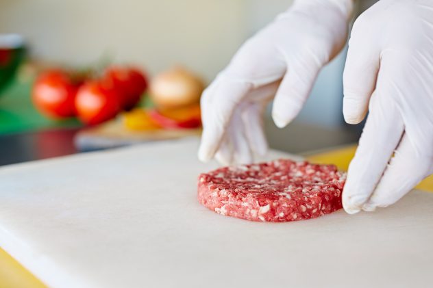 Hands in white gloves prearing a fresh hamburger patty beef meat burger making