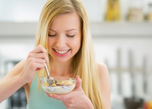 Happy young woman eating muesli in kitchen cereal