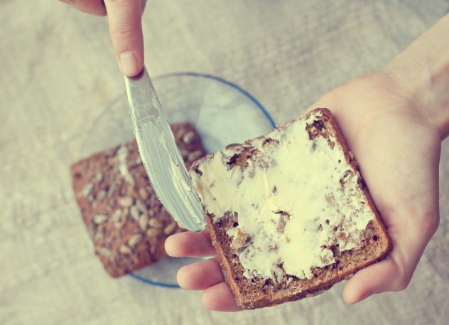 woman hand rubs butter on piece of rye bread margarine
