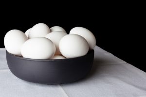 Näin valmistat munasta kokkelia rikkomatta kuorta White eggs in a black bowl on white linen napkin on black background from side off centre composition