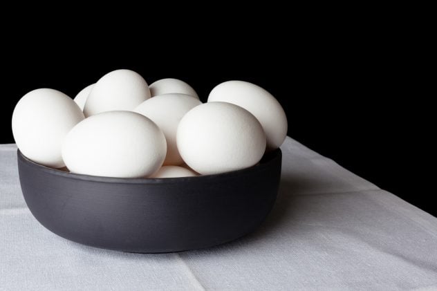 White eggs in a black bowl on white linen napkin on black background from side off centre composition