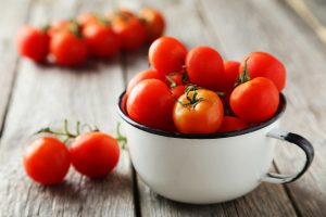 Fresh cherry tomatoes in cup on grey wooden background