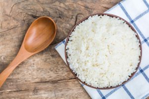 Cooked rice in bowl with spoon and dishcloth on old wooden table