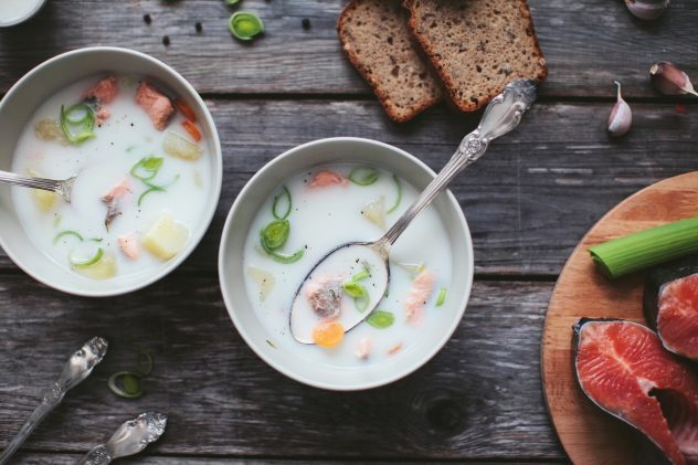 Finnish dairy ear with red fish in a plate with a spoon on a wooden table with bread, herbs and fish