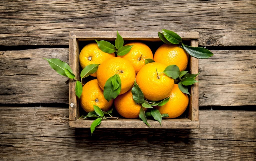 Oranges with leaves in an old box. On a wooden table. Top view