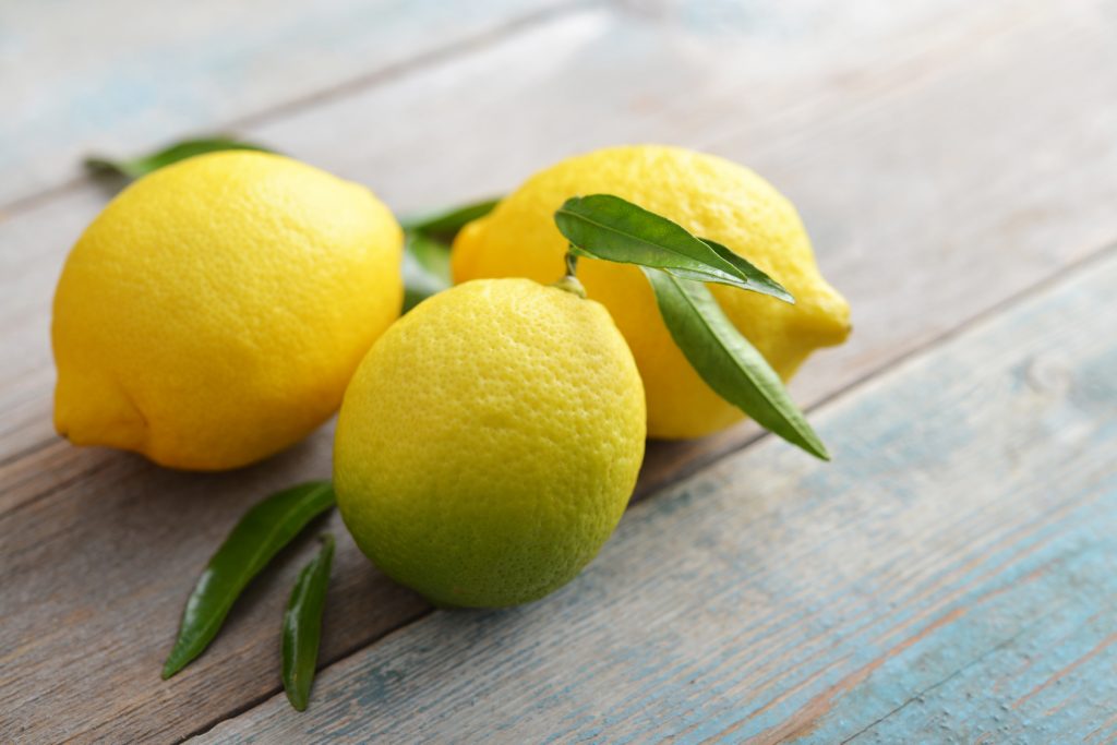 Fresh lemons with leaves on wooden background