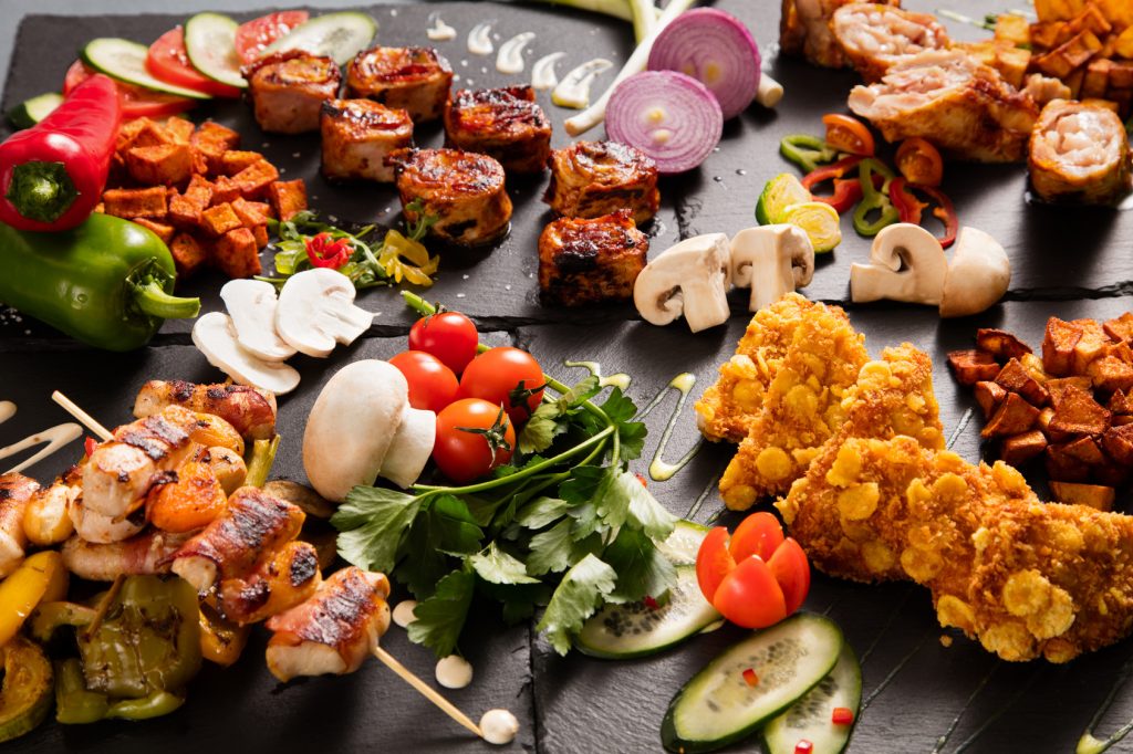 Delicious barbecued meat served on black stone plates decorated with vegetables and mushrooms