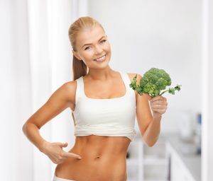 woman pointing at her abs and holding broccoli