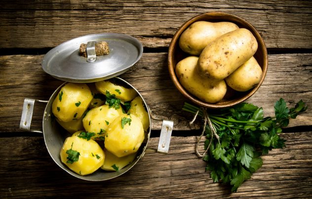 Boiled potatoes with herbs on wooden table .
