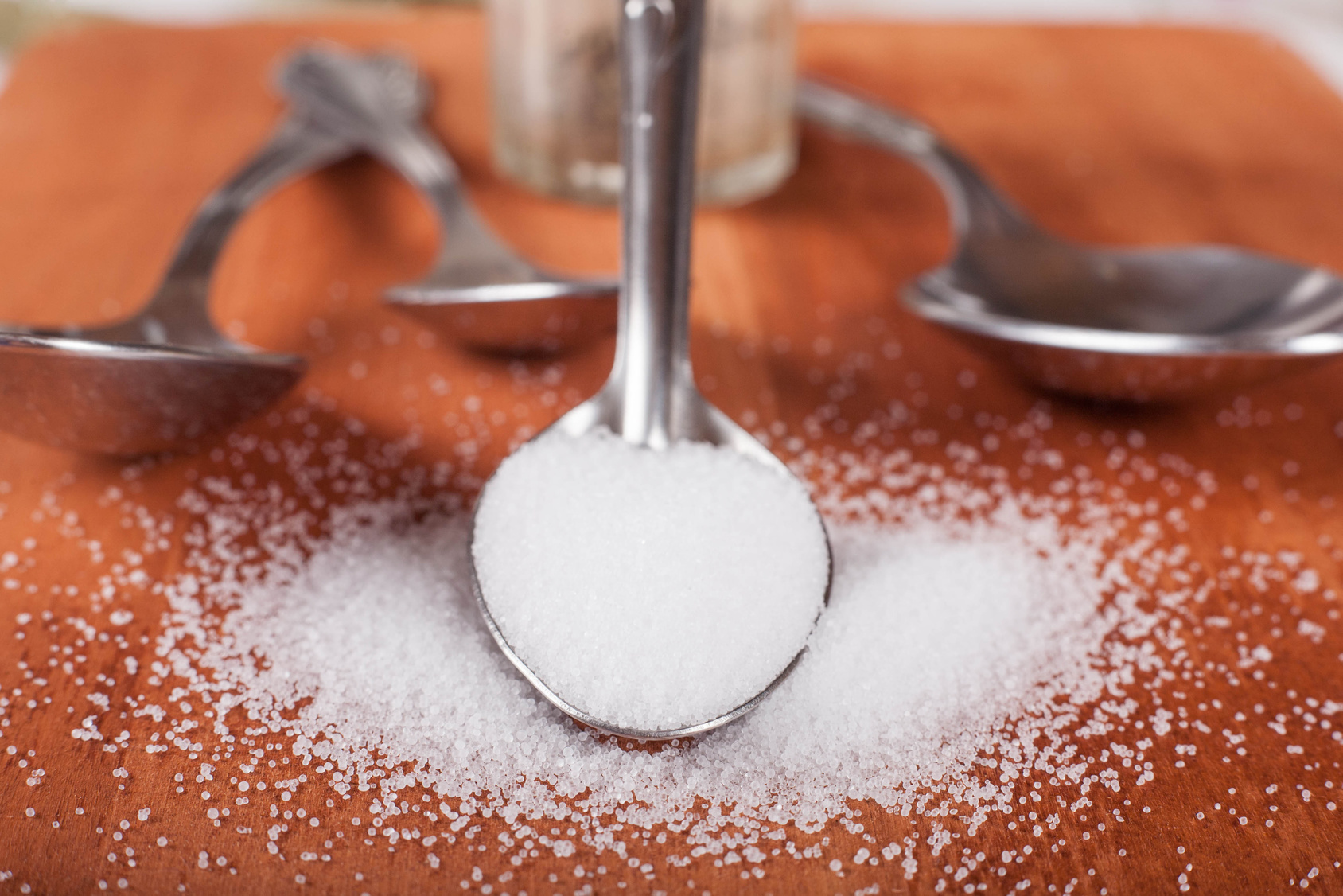 Close up shot of iodized table salt in metallic spoon next to three metallic spoons on wooden board