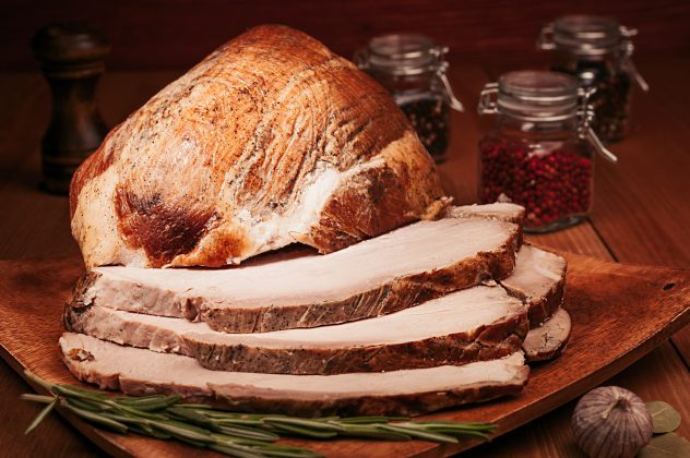 Christmas baked ham chopped slices on wooden board with spices.