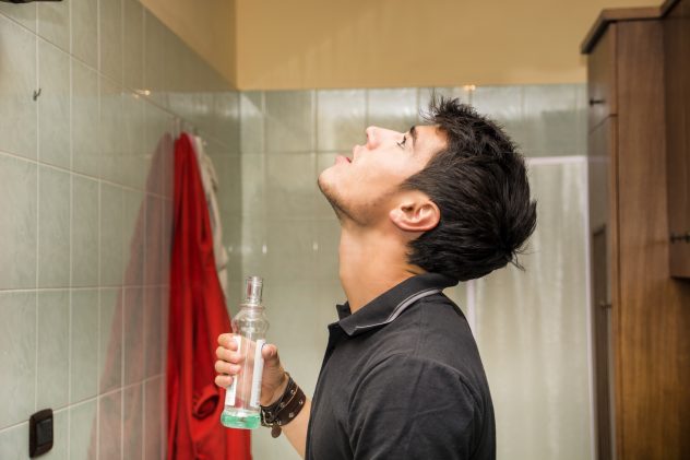 Handsome young man using mouthwash, in bathroom