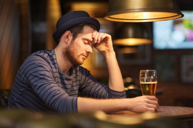 unhappy lonely man drinking beer at bar or pub