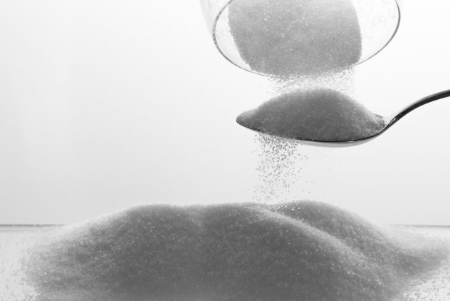 granulated sugar poured from glass trickling onto spoon
