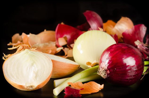 White, red and green onion with the husk on black wooden backgro