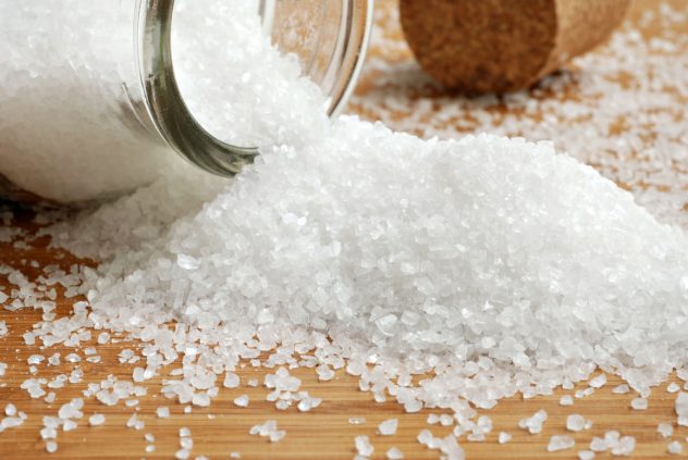 Sea salt spilling from glass bottle onto bamboo surface.  Cork b