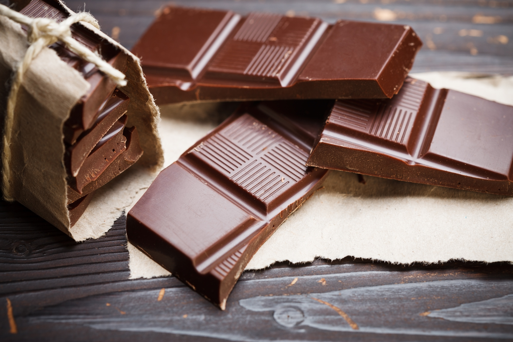 Pieces of chocolate with packing paper on wooden table, rustic style