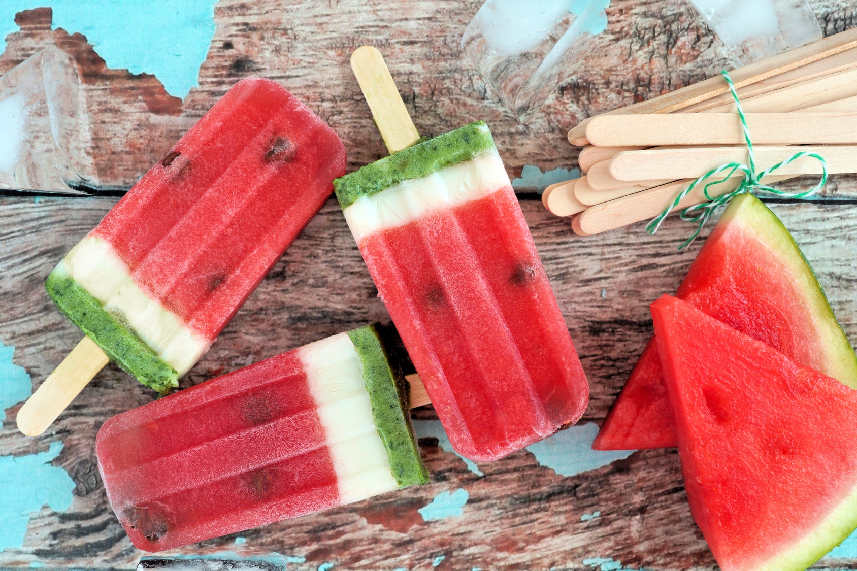 Homemade watermelon ice pops with melon slices against rustic wood background