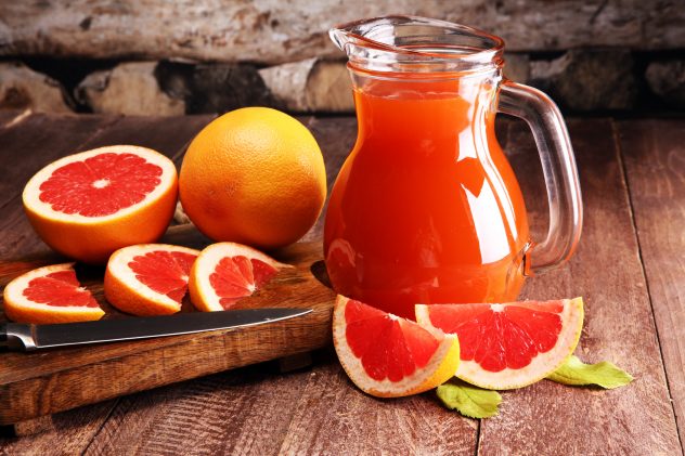 Grapefruit juice and ripe grapefruits on a wooden background