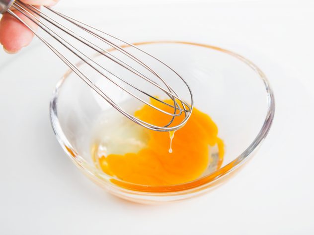 Whisk and egg in glass bowl