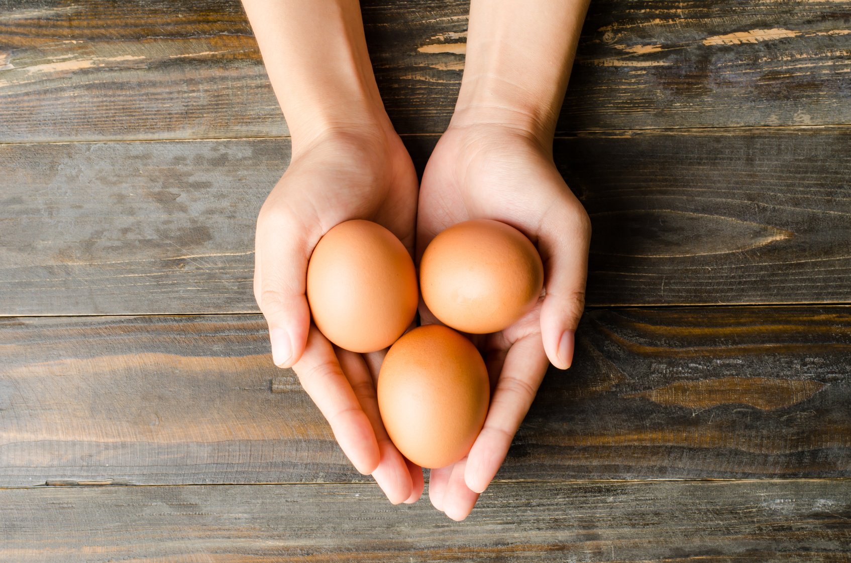 Fresh eggs are holding by hand on wooden background (food ingredient)