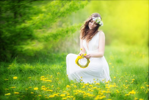 Image of pretty woman in a white dress weaves garland from dande