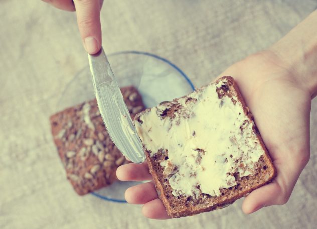 woman hand rubs butter on piece of rye bread