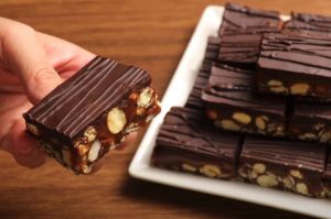 Nainen kaataa vuokaan pähkinöitä ja sulaa suklaata – lopputuloksena täydellinen DIY joululahja suklaa